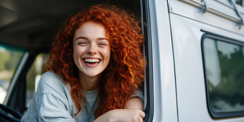 Young woman with long, curly red hair leaning out of a van window, laughing joyfully and embracing the thrill of a carefree road trip adventure through beautiful landscapes