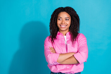 Obraz premium Charming young woman in a pink shirt with curly hair smiling against a vibrant blue background, exuding confidence and style.