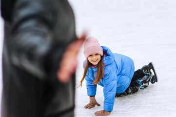 Little smiling girl, child slipped and lies on ice on skating rink in winter in skates. Photography, portrait, sport and hobby concept.