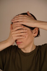 A woman covers her face with her hands on a white background. Close up.
