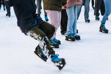 Happy adult stylish people skating, falling and slipping on rink in winter outdoors. Photography, legs close-up, sport and hobby concept.