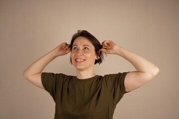 Portrait of a young happy woman touching her ear on gray background.