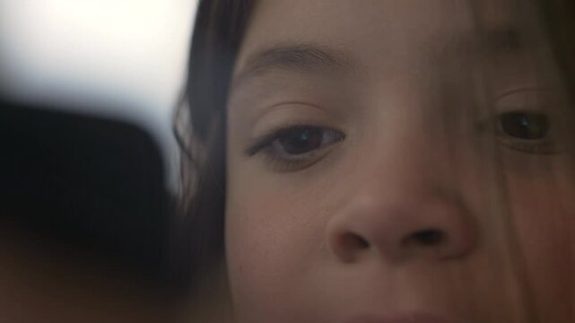 Close-up of child's eyes staring at phone screen consuming media online. Little girl eyesight hypnotized by modern technology looking at smartphone device