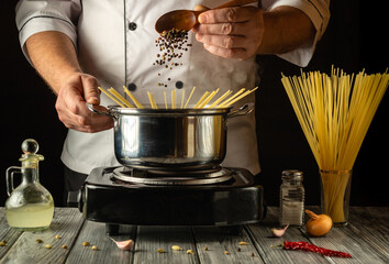 A skilled chef adds black peppercorns to a pot of boiling pasta, creating a flavorful dish. The...