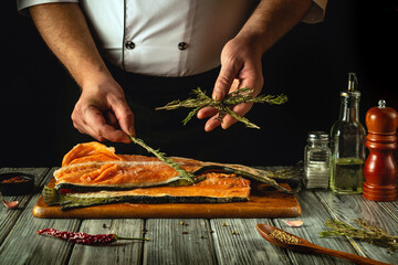 A chef meticulously arranges fresh salmon on a wooden cutting board, skillfully adding fragrant herbs. The kitchen is dimly lit, highlighting the vibrant colors of the fish and ingredients