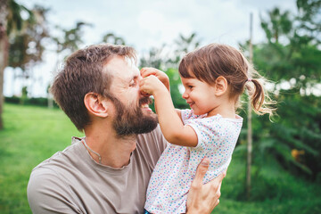 Father and young daughter sharing a playful and joyful moment outdoors in green park, expressing...