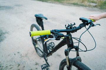A close-up view of a black mountain bikes handlebars with yellow grips. The bike is parked on a dirt road. The handlebars have a brake lever, a gear shifter, and a phone holder.
