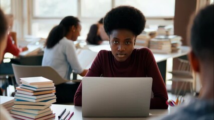 Focused student working in busy library with books and laptops in collaborative study environment