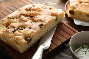 Pieces of delicious focaccia bread with olives, thyme, salt and knife on wooden table, closeup