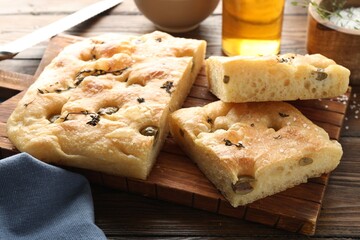 Pieces of delicious focaccia bread with olives, thyme and salt on wooden table, closeup