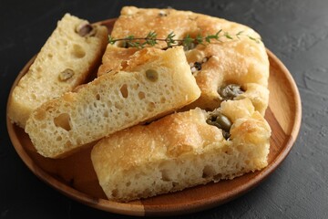Slices of delicious focaccia bread with olives, thyme and salt on black table, closeup