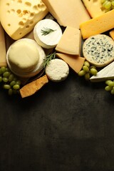 Different types of cheese, rosemary and grapes on dark textured table, flat lay. Space for text