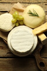 Different types of cheese, rosemary and grapes on wooden table, top view