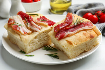 Pieces of delicious focaccia bread with bacon served on white table, closeup