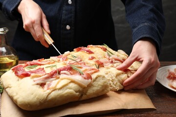 Woman cutting delicious focaccia bread at wooden table, closeup