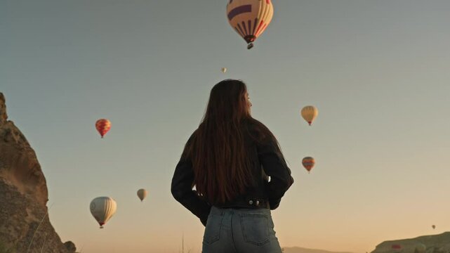 Silhouette of a young beautiful woman and lots of flying Hot Air Balloons. A fairy tale at dawn in Cappadocia, Turkey. Travel tour Adventure Happy moments of life Inspiration Admiration Low angle shot