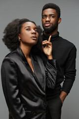 Stylish black couple poses elegantly with confidence against a neutral background, showcasing modern fashion and expressive emotions in a contemporary setting