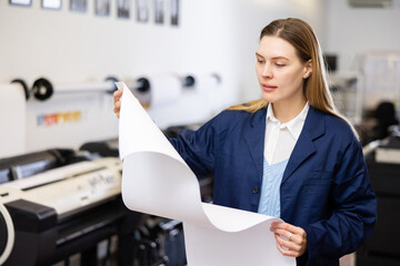 Woman looking at large format paper while working in printing office.