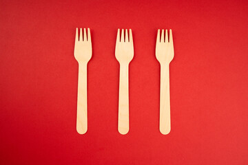 Three wooden eco-friendly forks vertically on red background