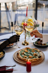 Elegant toast with white wine at a candlelit dinner, celebrating with gourmet pizza and fine dining