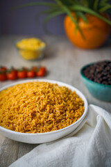 Global rice dishes array on rustic table, featuring Indian Puliyogare, Latin Arroz con Pollo, and West African Jollof rice with fresh vegetables and spices, ideal for culinary articles and menus.