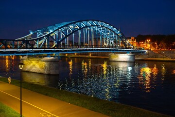 Beautiful illuminated bridge over the Vistula River in Krakow on a calm night with reflections on the water