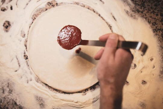 A man prepares a pizza and spreads sauce