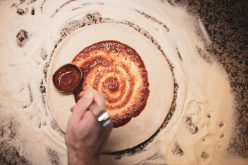 A man prepares a pizza and spreads sauce