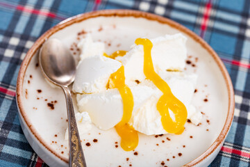 Slice of fresh farm cottage cheese, filled with large amount of liquid summer honey, is served on snow-white plate