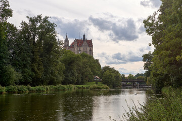 Obraz premium Picturesque Schloss Hohenzollern Castle Overlooking Tranquil River and Historic Bridge in Scenic German Countryside