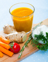 Freshly squeezed carrot juice served with ginger, fresh vegetables and cream on wooden board