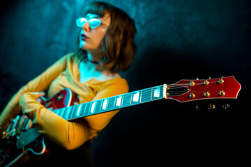 Fashion young hipster woman with curly hair with red guitar in neon lights. Rock musician posing...
