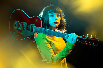 Obraz premium Hipster woman with curly hair play red guitar in neon lights. Rock musician is playing electrical guitar.