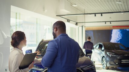 Saleswoman selling pre owned vehicles to client after assessing condition and providing information, addressing customer concerns about reliability and maintenance of used car, camera B