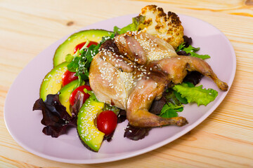 Image of quail-tobacco with sesame which served with salad of avocado and greenery on the plate indoors.