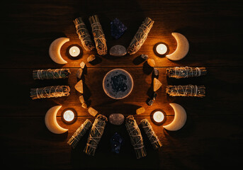Smudging herbs, crystals, candles, and moon shapes arranged on a wooden table, creating a mystical atmosphere for spiritual practices
