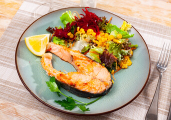 Fried salmon steak with a light vegetable salad made from corn, lettuce leaves and grated beetroot, served with a ..slice of lemon
