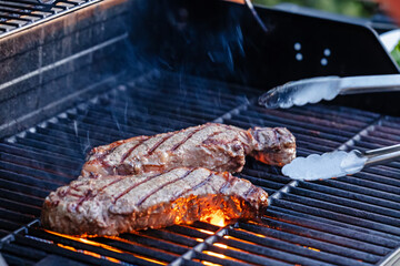 Two thick steaks sizzle over an open flame on a backyard grill