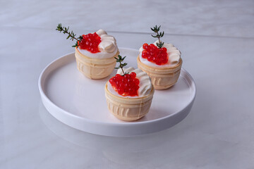 Tartlets with salmon caviar. In waffle cups with boiled egg and mayonnaise. On white flat plate with rim, with sprigs of fresh thyme