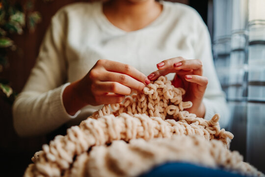 Close up of young woman's hands knitting blanket with her fingers by the window	
