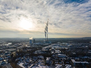 Fototapeta premium Industrial landscape with smokestacks emitting smoke at sunset near a city in winter