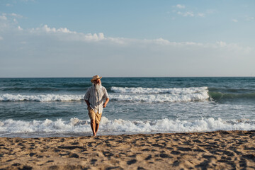 An elderly man strolling along the beach, enjoying the soothing sound of ocean waves under the warm afternoon sun, representing a peaceful and serene moment in nature