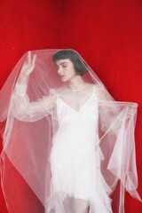 Woman wearing a sheer veil poses against a vivid red background during a fashion photoshoot in a...