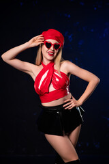 Beautiful sexy girl in red latex top, black latex skirt and red beret with red heart-shaped glasses. Smiling and posing on dark background. Holding glasses with hand