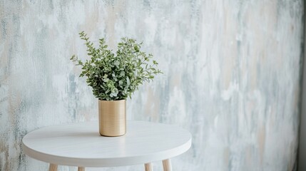 A small gold vase with fresh greenery on a round white table, with an accent wall featuring textured wallpaper and modern lighting