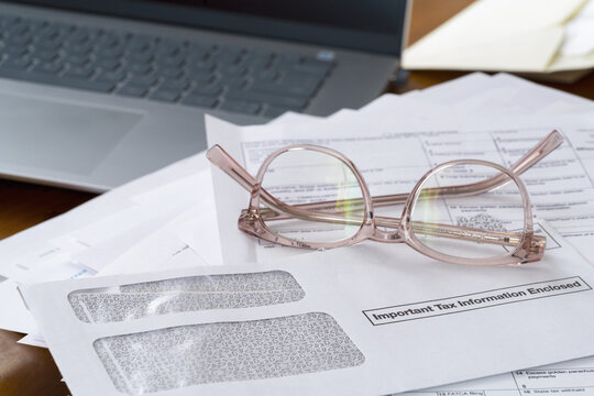 Desk with laptop, reading glasses, documents tax forms and envelope saying Important Tax Information Enclosed. Income Tax preparation concept.