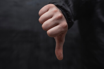 Customer's hand in shirt showing thumb down, close-up on dark background. Service evaluation and a...