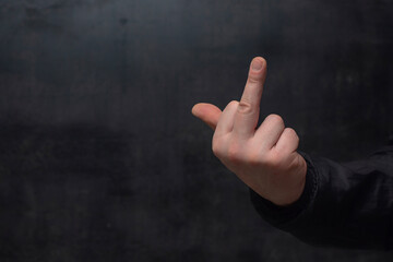 Man in a shirt showing a crude fuck gesture, middle finger sign, close-up against a concrete wall.