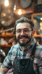 Obraz premium A smiling young man with a beard wearing glasses and a plaid shirt, stands in front of a blurry background.