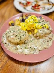 Biscuits and Sausage Gravy, Scrambled Eggs, and Fried Potato Medley for Breakfast on a Pink Plate at a Restaurant